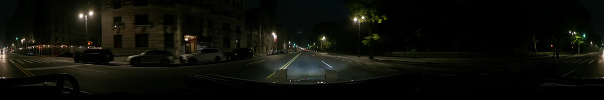 From a car's point of view, a wide road in New York is flanked by streetlights and city buildings on a spring night in the United States.