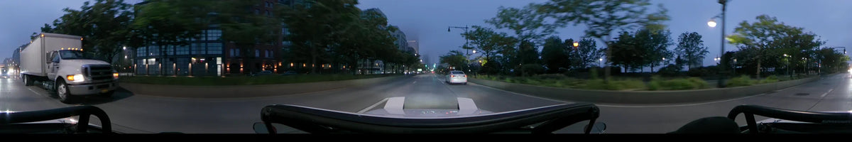 Driving through the fog at dawn, a car follows another vehicle along a New York road lined with spring greenery and buildings in the United States.