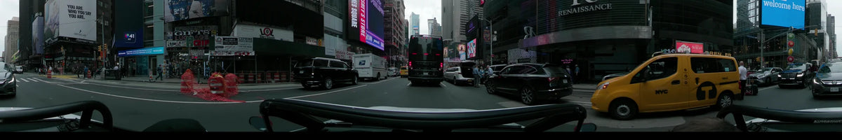 A car drives through Times Square in New York on an overcast spring day, surrounded by bright billboards, city traffic, and a white USPS delivery truck.