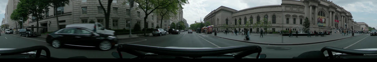A car drives past the New York Public Library and colorful food trucks on an overcast spring day in New York, surrounded by lush green trees.