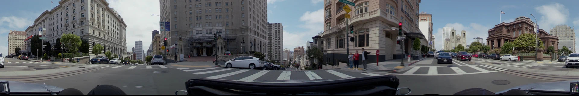A steep city street in San Francisco featuring tall buildings, parked cars, and a pedestrian crossing under a partly cloudy sky.