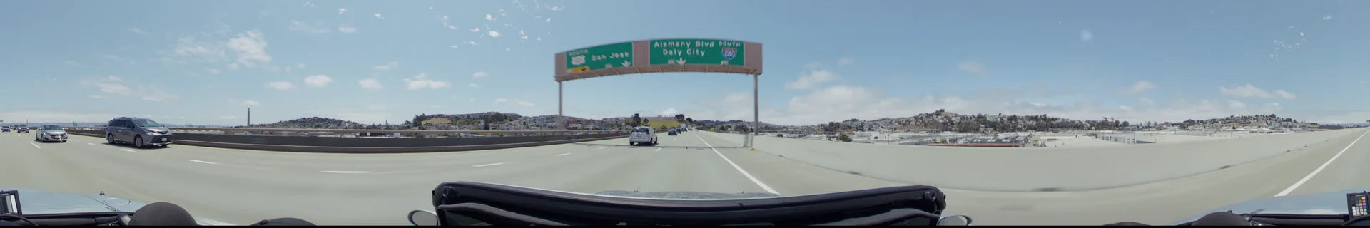 A multi-lane highway in San Francisco with overhead signs for Alemany Blvd, Daly City, and San Jose, featuring light traffic and residential hills in the distance.