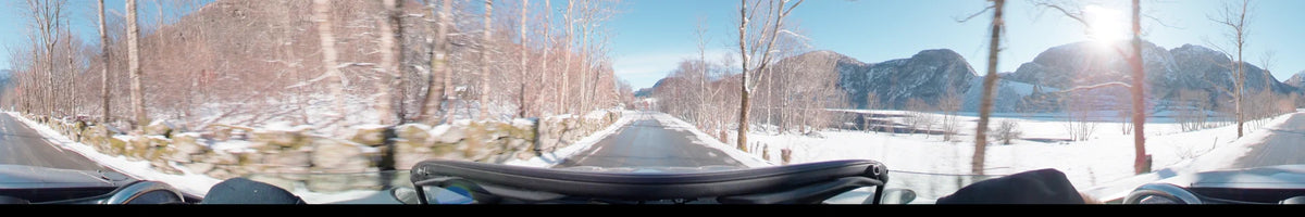 On a clear spring day in Stavanger, Norway, this view from a car shows a snow-covered road flanked by a stone wall and leafless trees.