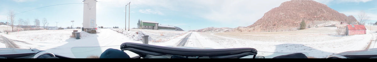 Long buildings and distant hills line the snow-dusted road in this view from a car in Stavanger, Norway, on a partly cloudy spring day.