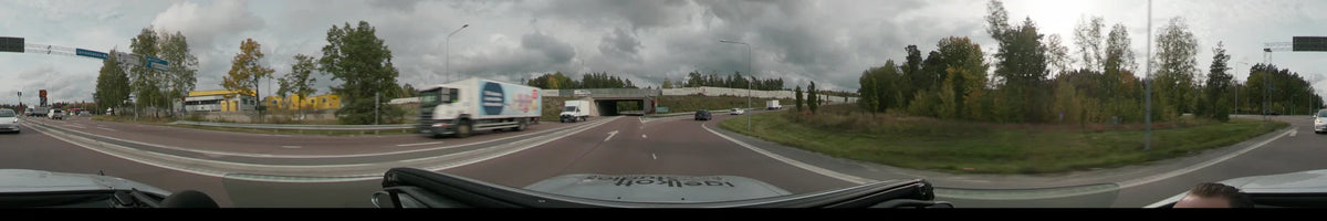 A truck and a white car precede a vehicle driving on a highway in Stockholm, Sweden, during an overcast autumn day, surrounded by colorful trees and rocks.