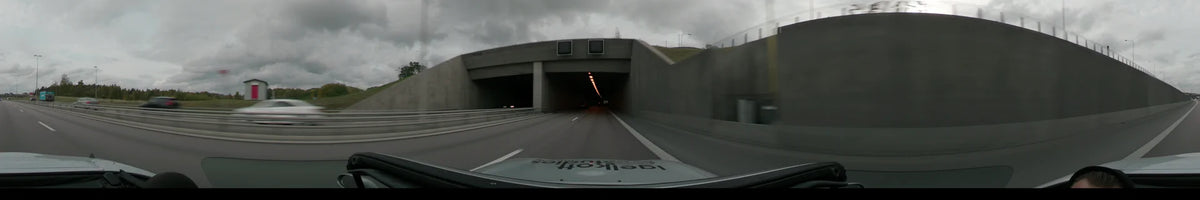 A car drives into a concrete tunnel in Stockholm, Sweden, on an overcast autumn day. Grey concrete walls flank the road leading into the tunnel.
