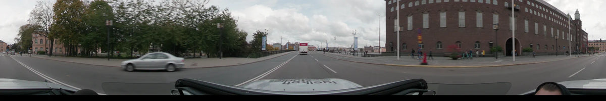 A white truck leads the way across a bridge in Stockholm, Sweden. City buildings and autumn foliage are visible under a gray, overcast sky.
