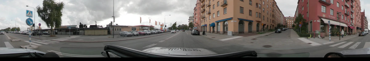 Yellow buildings with blue awnings and a line of orange flags flank a city street in Stockholm, Sweden, as a car drives during an overcast autumn day.