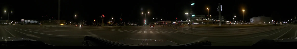 A car navigates an urban street in Stockholm, Sweden, during a clear autumn night, with a zebra crossing and red traffic lights visible ahead.