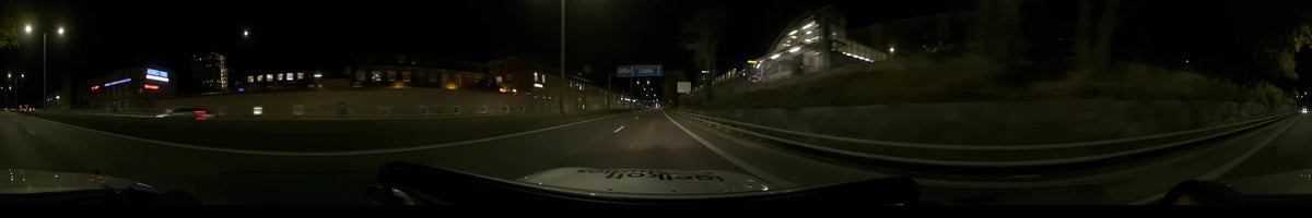 During a clear autumn night in Stockholm, Sweden, a car drives along a city road past illuminated buildings and blue overhead signs.