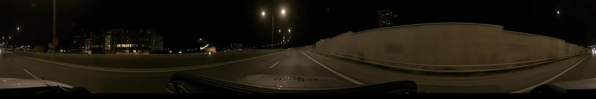 On a clear autumn night, a car travels a road in Stockholm, Sweden, beside a high wall and rows of streetlights.