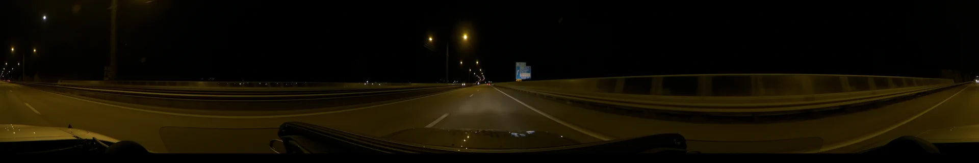 A blue E20 road sign and glowing streetlights line a highway in Stockholm, Sweden, as a car drives along on a clear autumn night.