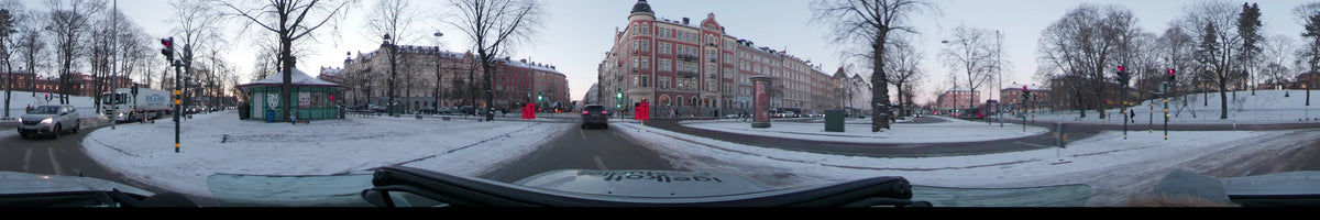 Ornate red buildings and road signs flank a slushy street in Stockholm, Sweden, as a car drives during a clear winter dawn.