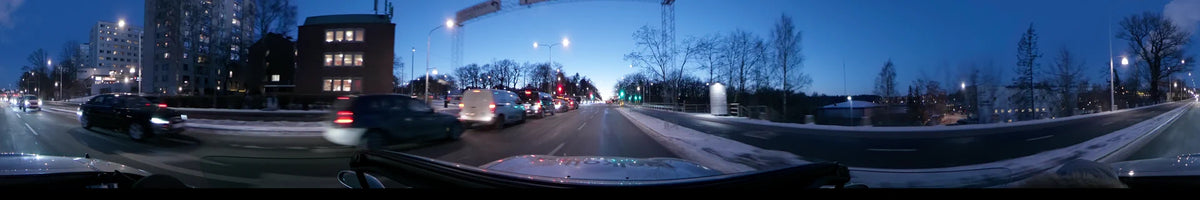 White vans and city traffic occupy the road as a car travels past snowy banks and bare trees in Stockholm, Sweden, during a clear winter sunset.