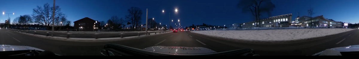 In Stockholm, Sweden, a car drives along a snowy road illuminated by bright streetlights and red taillights under a clear winter sunset.