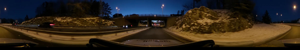 A car travels beneath a concrete overpass and past snowy embankments in Stockholm, Sweden, while a clear winter sunset illuminates the sky.