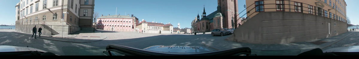 A car drives through Stockholm, Sweden, on a clear spring day, passing by the Storkyrkan church and the historic buildings of Gamla Stan.
