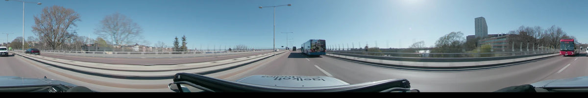 On a clear spring day in Stockholm, Sweden, a car follows a blue bus across a wide bridge lined with street lamps.