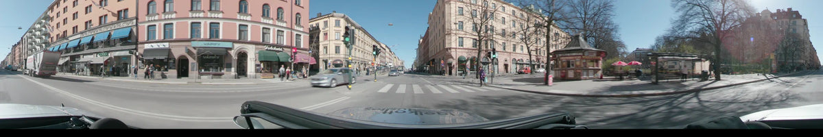 Multi-story buildings and green traffic lights are visible from a car in Stockholm, Sweden, during a clear spring day, passing a white pedestrian crosswalk.