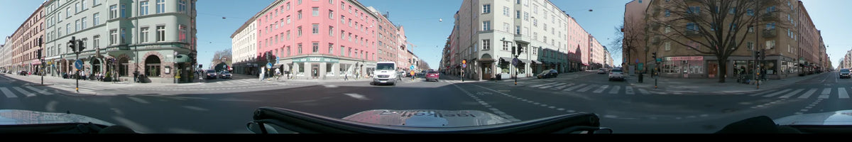 A white van and a red car led the way down a Stockholm, Sweden, city street flanked by pink and green buildings on a clear spring day.