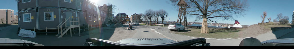 Construction signs and parked cars accompany a drive through Stockholm, Sweden, on a clear spring day, past red brick buildings and bare trees.