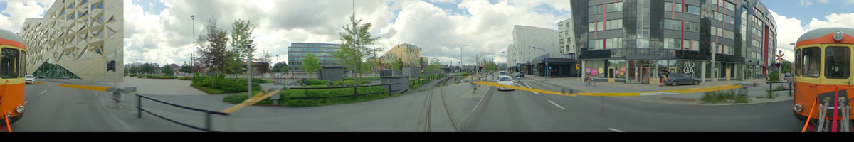 View from a car in Uppsala, Sweden, on a partly cloudy summer day. The scene features train tracks, a modern yellow building, and white urban architecture.