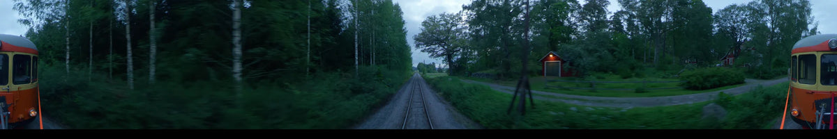 View from a train moving along railway tracks through a lush summer forest in Uppsala, Sweden, under a partly cloudy afternoon sky.