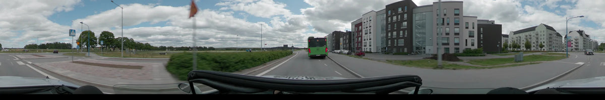 A green bus travels along a road in Uppsala, flanked by modern apartment buildings on the right and green hedges on the left.
