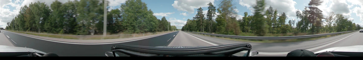 A straight road in Upplands-Bro is flanked by dense green pine forests and a metal guardrail under a partly cloudy sky.