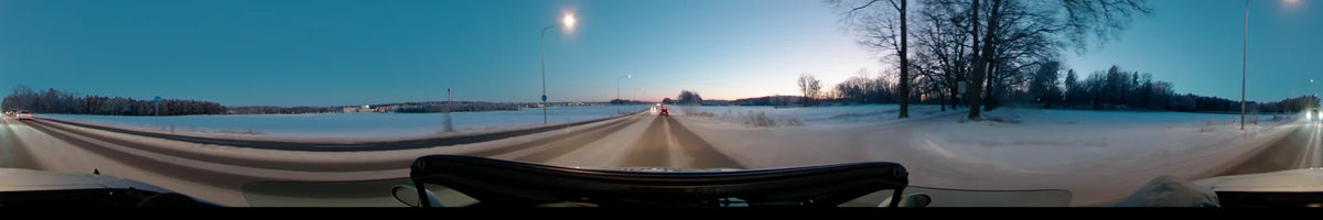 Street lamps and a red car accompany this drive through Uppsala, Sweden, on a clear winter afternoon, crossing a road bordered by vast snowy fields.