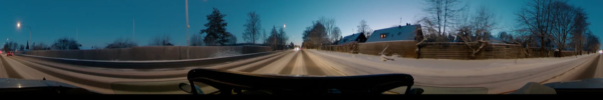 Residential houses and bare trees line a snowy road in Uppsala, Sweden, on a clear winter afternoon as a car drives along the route.