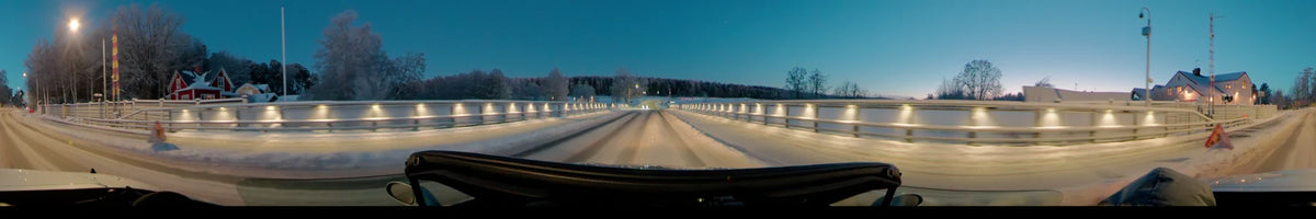 Crossing a bridge in Uppsala, Sweden, on a clear winter afternoon, the car passes illuminated railings and a horizon of snow-covered trees.