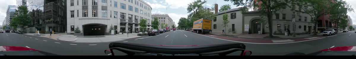 A yellow Penske truck and white stone buildings flank the street as a car travels through Washington, United States, on a partly cloudy spring day.