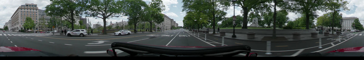 Constitution Avenue in Washington, United States, is lined with green trees and the US Department of Justice building as a car moves on a partly cloudy spring day.