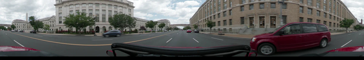 Monumental stone buildings and a distant bridge are visible as a car travels through Washington, United States, on a partly cloudy spring afternoon.