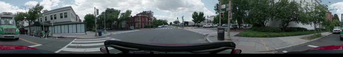In Washington, United States, a car drives past red brick buildings and a wide pedestrian crosswalk during a partly cloudy spring afternoon.