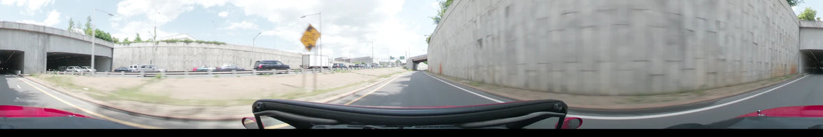 During a partly cloudy spring afternoon in Washington, United States, a car drives alongside a concrete wall toward an overpass with highway traffic nearby.