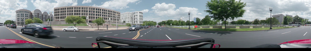 The US Capitol dome is visible in the distance while a car drives along a broad road in Washington, United States, on a partly cloudy spring afternoon.