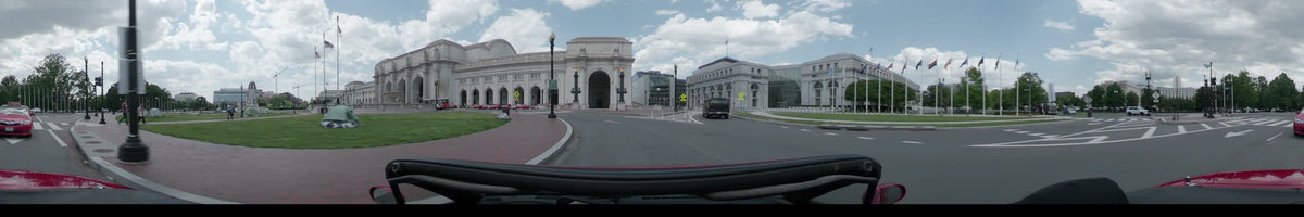 A car approaches the grand facade of Union Station in Washington, United States, on a partly cloudy spring afternoon along a wide city road.