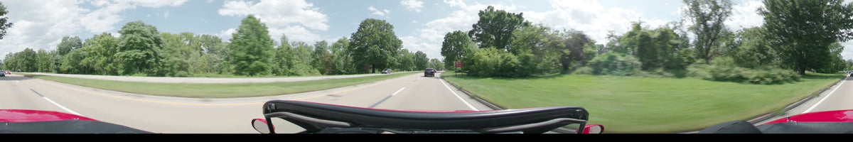 Lush green foliage lines a road in Washington as a car follows another vehicle under a partly cloudy spring afternoon sky.