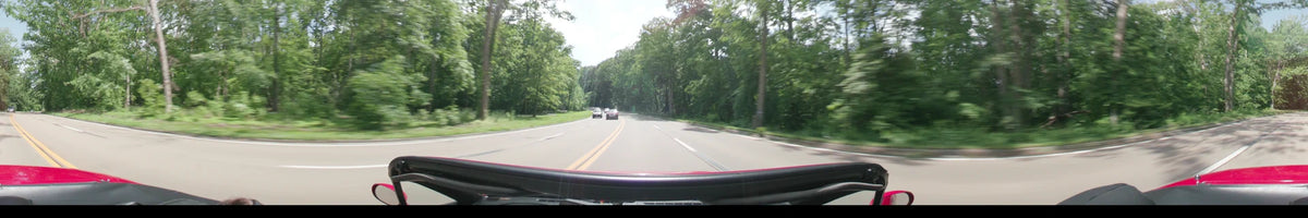 Dense spring greenery flanks a divided highway in Washington where a car travels behind other vehicles during a partly cloudy afternoon.