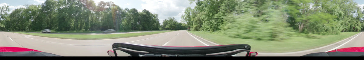 Under a partly cloudy afternoon sky in Washington, a car travels along a multi-lane road that is bordered by lush green spring trees.
