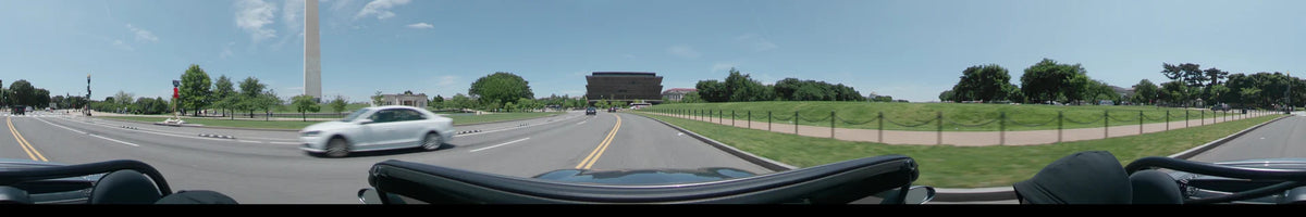 Past the National Museum of the American Indian, a car drives through Washington, United States, on a clear spring day surrounded by lush greenery.