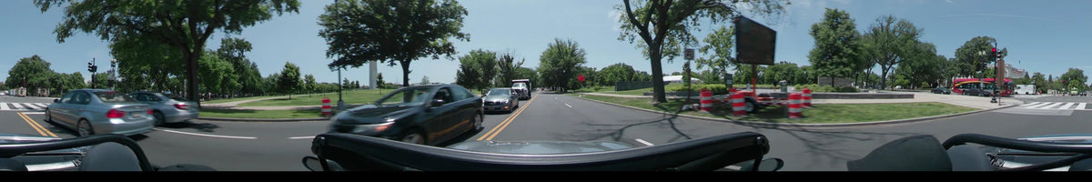 Lush greenery, other vehicles, and the Vietnam Veterans Memorial are visible in Washington, United States, on a clear spring day from a car.