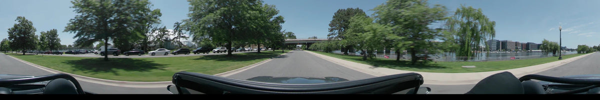 Under a bridge, a car drives through Washington, United States, on a clear spring day, past lush green trees and a waterfront.