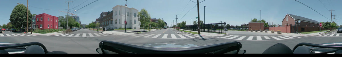 Green trees and a white building flank a road in Washington, United States, as a car crosses a pedestrian walkway on a clear spring day.
