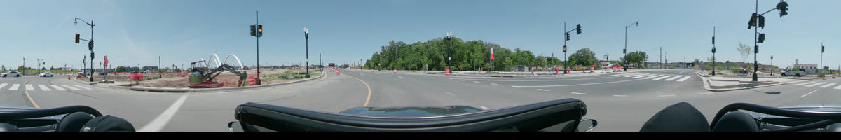 Orange traffic cones line a multi-lane road in Washington, United States, as a car drives past green trees on a clear spring day.