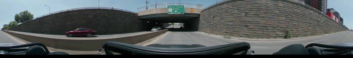 Between textured stone walls, a car travels under a South Capitol Street sign in Washington, United States, on a clear spring day.