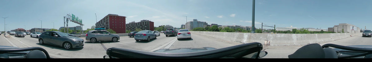 Modern urban buildings and green trees are visible from a car traveling along a multi-lane road in Washington, United States, on a clear spring day.