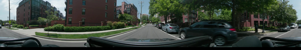 Lush green trees and red brick apartment buildings line a residential street in Washington, United States, as a car proceeds on a clear spring day.